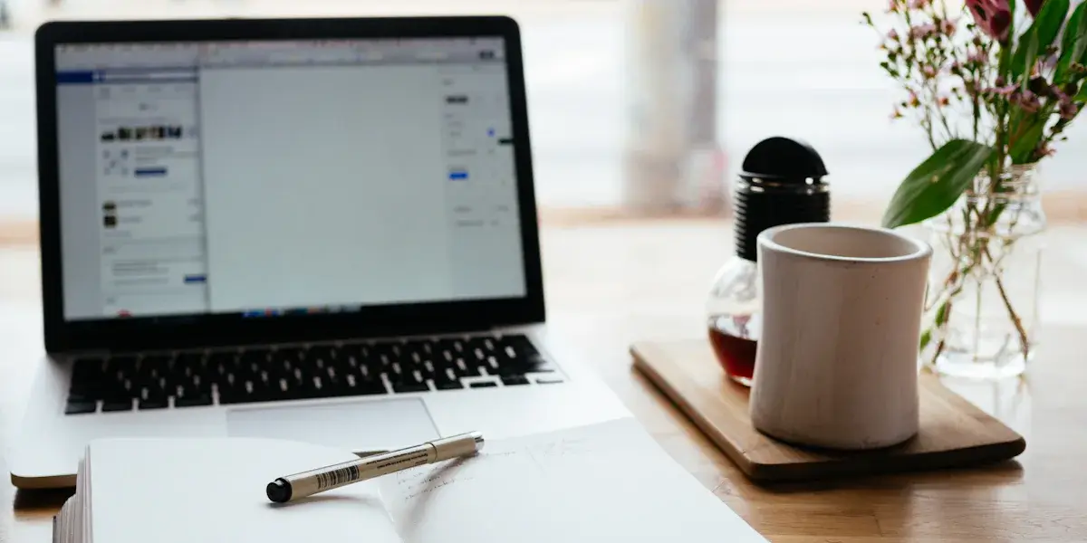 Portátil abierto sobre un escritorio con una taza de café y unas flores