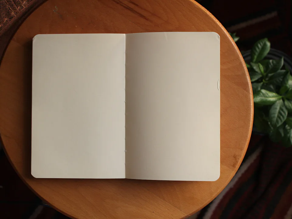 Libreta abierta sobre una mesa redonda de madera junto a una planta