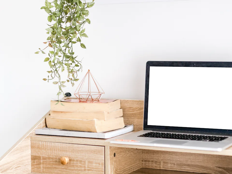 Portátil sobre una mesa con libros apilados y una planta colgante