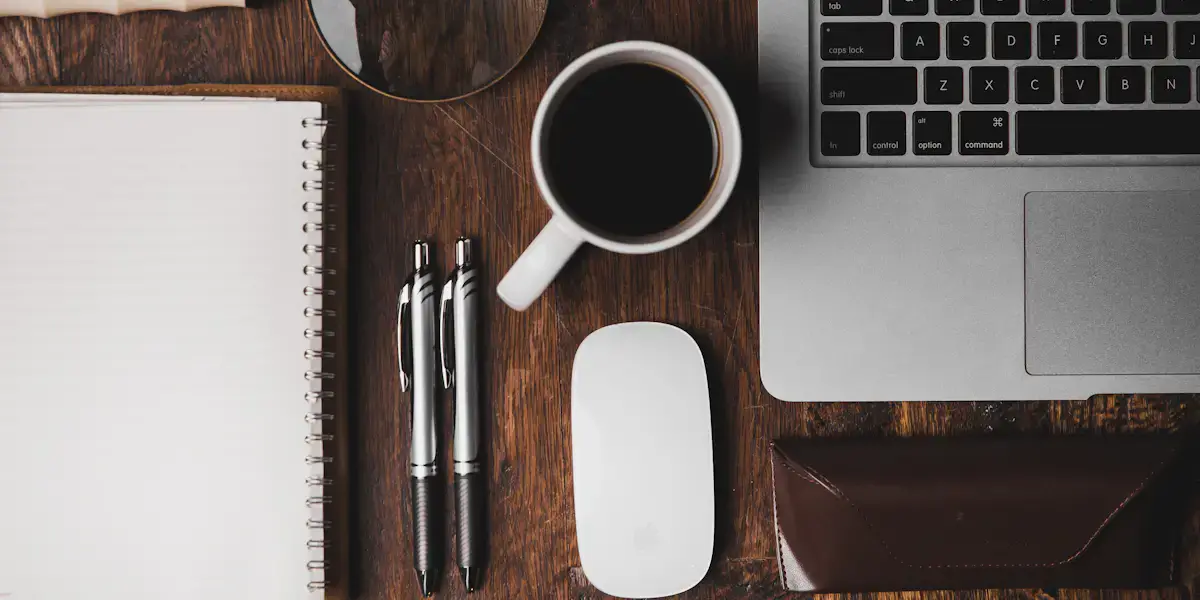Libreta, taza de café, bolígrafos y un teclado sobre una mesa de madera