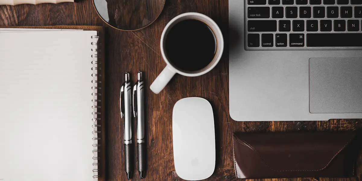 Libreta, taza de café, bolígrafos y un teclado sobre una mesa de madera